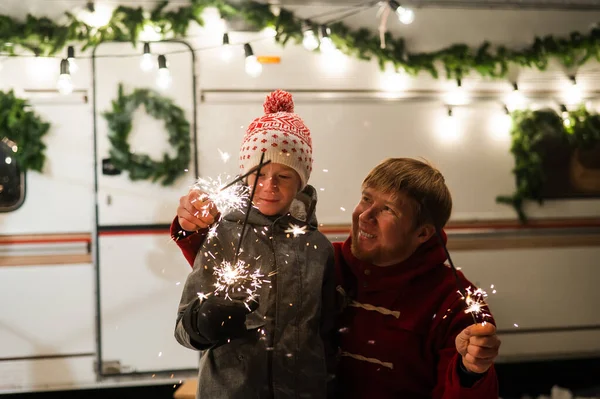Vit rödhårig man med en pojke som håller i tomtebloss i husbilen. Far och son firar jul på en resa. — Stockfoto