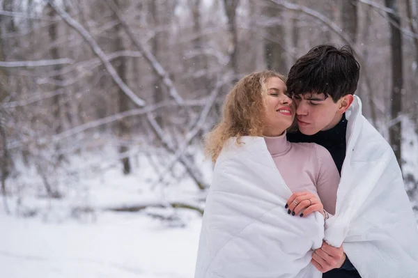 Ett ungt par går i parken på vintern. Killen och flickan kysser varandra i en vit filt utomhus.. — Stockfoto