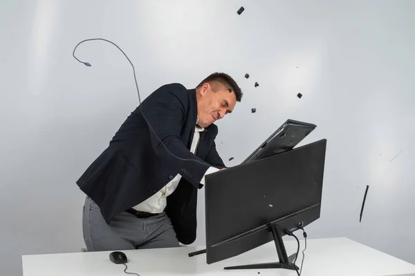 Caucásico hombre en un traje se enoja y rompe el teclado en el monitor. Un oficinista furioso rompe el ordenador. —  Fotos de Stock