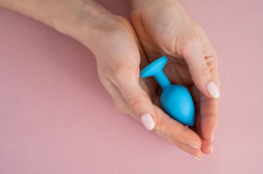 Bir kadın pembe arka planda mavi anal bir tıpa tutuyor. Alternatif seks için yetişkin oyuncağı