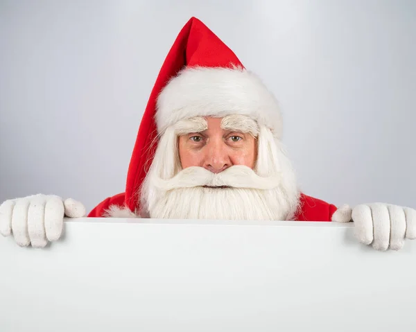 Santa Claus mira por detrás de un anuncio sobre un fondo blanco. Feliz Navidad.. — Foto de Stock