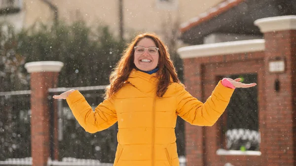 Rödhårig vit kvinna jublar på vintern och fångar snöflingor med handflatorna. — Stockfoto