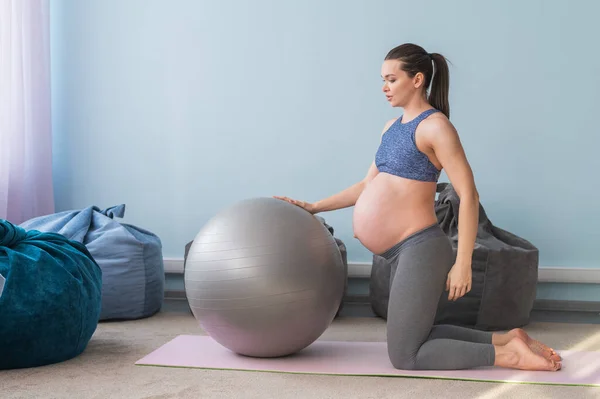 Zwangere Europese vrouw voert oefeningen met fitness bal. Verwachte moeder doet yoga in het derde trimester. Meisje in de klas ter voorbereiding op de bevalling. — Stockfoto