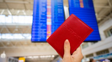 Havaalanı bilgi panosunun arka planında pasaportu olan bir kadın..