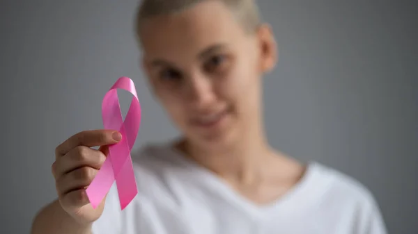 Uma mulher sem rosto usando uma camiseta branca segura uma fita rosa como um símbolo de câncer de mama em um fundo branco. — Fotografia de Stock