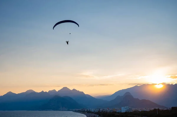 Silhueta de um homem em um parapente voando sobre o mar ao pôr do sol. — Fotografia de Stock