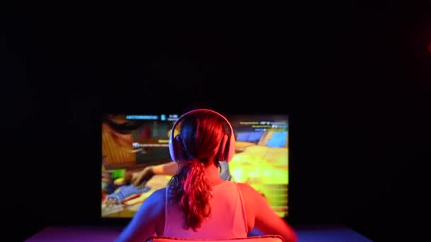 Biała kobieta raduje się z wygrania gry komputerowej w neonowym świetle w ciemności. — Wideo stockowe