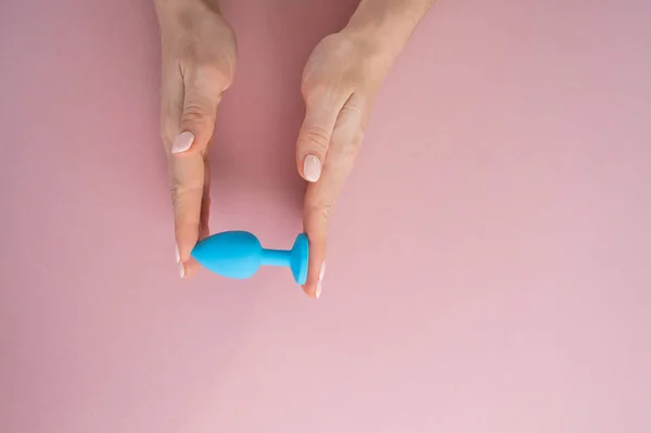 Una mujer sostiene un tapón anal azul sobre un fondo rosa. Juguete para adultos para sexo alternativo — Foto de Stock