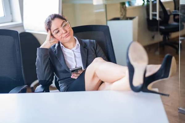 Geschäftsfrau legte Füße auf Schreibtisch und benutzte Handy im Büro — Stockfoto