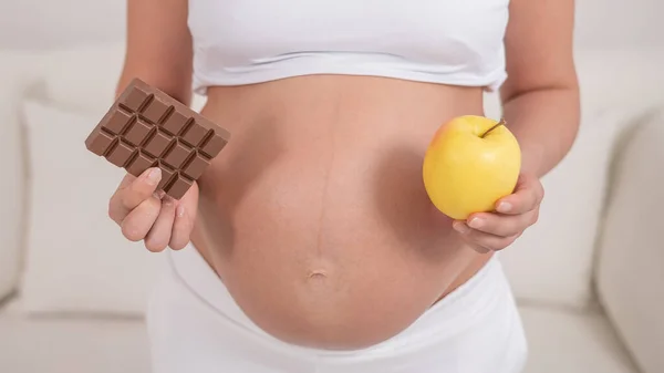 Hamile bir kadın bir elma ve çikolata tutuyor. Hamileliğin dokuzuncu ayı. — Stok fotoğraf
