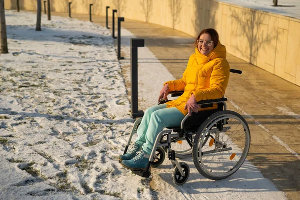 Blanke vrouw met een handicap rijdt in de winter op een stoel in het park. Meisje op een wandeling in een rolstoel. — Stockfoto