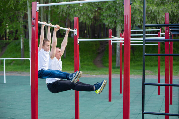 Caucasian man trains a boy on the horizontal bar on the playground. Dad and son go in for outdoor sports.