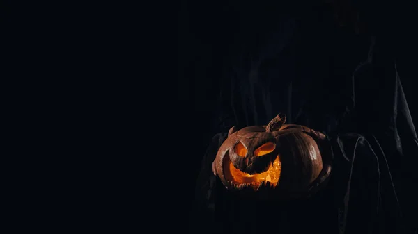 Häxan håller en pumpa jack o lykta glöder i mörkret. Halloween. — Stockfoto