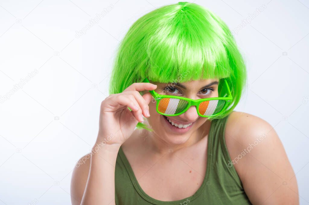 Cheerful young woman in green wig and funny glasses celebrating st patricks day on a white background