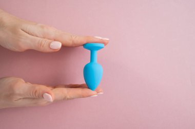 Bir kadın pembe arka planda mavi anal bir tıpa tutuyor. Alternatif seks için yetişkin oyuncağı