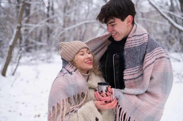 Um jovem casal caminha no parque no inverno. O tipo e a rapariga estão a beber uma bebida quente ao ar livre.. — Fotografia de Stock