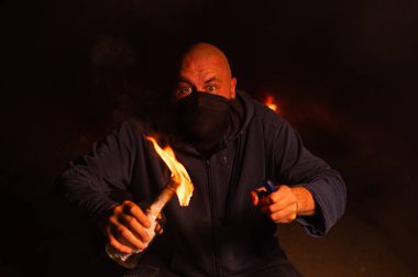 Maskeli bir adam yanan bir şişe tutuyor. Molotof kokteyli.