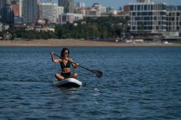 Mujer caucásica está montando una tabla de SUP en el río en la ciudad. Deportes de verano. — Foto de Stock