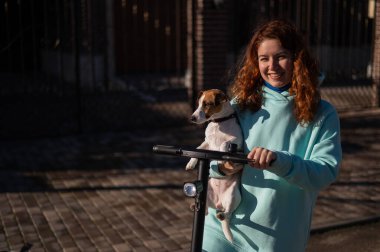 Kızıl saçlı bir kadın köpek Jack Russell Terrier ile kır evinde elektrikli scooter kullanıyor..