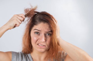 Tüyleri diken diken olmuş beyaz bir kadın elinde bir tutam saçla. Saç kaybı ve kadın saç dökülmesi..