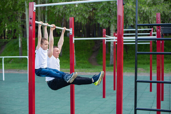 Caucasian man trains a boy on the horizontal bar on the playground. Dad and son go in for outdoor sports.