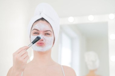 Saçında havlu olan güzel beyaz kadın kilden bir maske takıyor. Evdeki güzellikle ilgilenmek.
