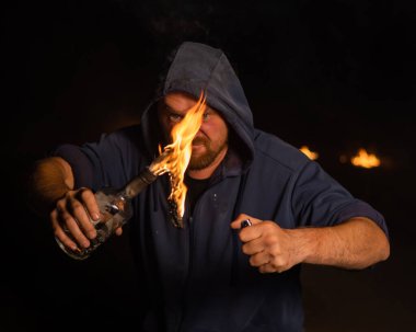 Kapüşonlu adam yanan bir şişe tutuyor. Molotof kokteyli.
