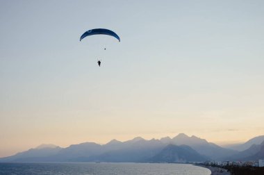 Gün batımında denizin üzerinde uçan bir adamın silüeti..