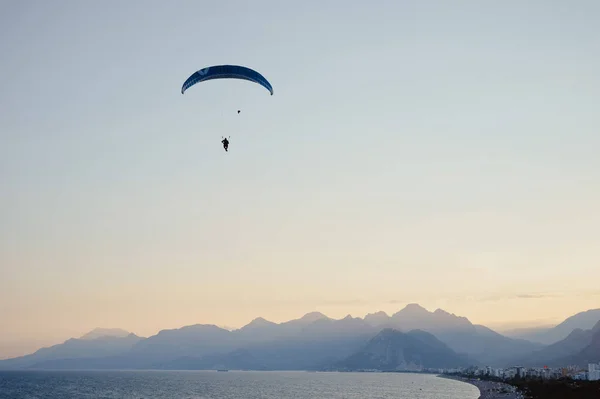 Silhueta de um homem em um parapente voando sobre o mar ao pôr do sol. — Fotografia de Stock