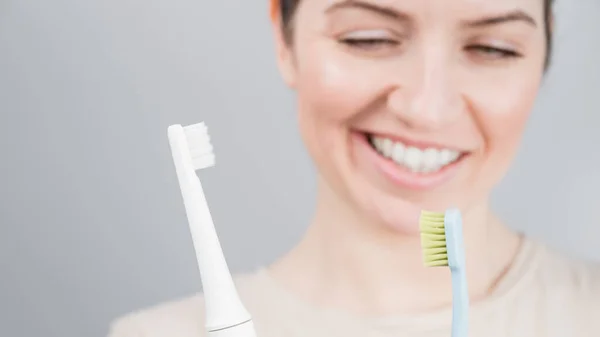 Happy woman compares a toothbrush with an electric one. The girl chooses oral hygiene products — Stock Photo, Image