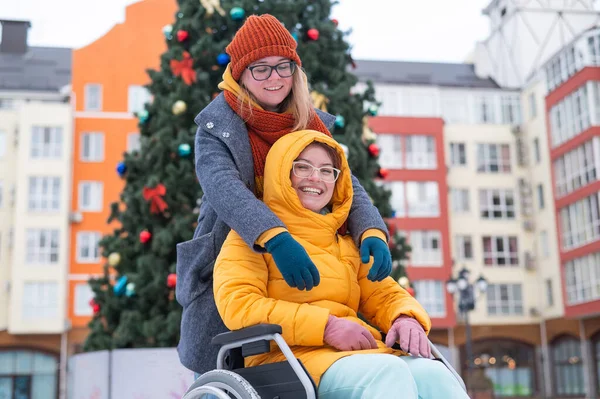 Vit kvinna kör sin vän i rullstol vid julgranen. — Stockfoto