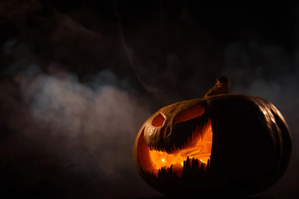 Een griezelige pompoen met een gesneden grimas in de rook. Jack o lantaarn in het donker. — Stockfoto