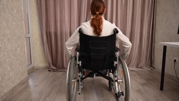 Femme blanche dans un fauteuil roulant conduit jusqu'à la fenêtre et ouvre les rideaux. — Video