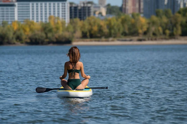 Běloška jede na SUP prkně na řece ve městě. Letní sport. — Stock fotografie