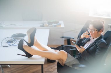 İş kadını ayaklarını çalışma masasına koydu ve ofiste cep telefonu kullandı.