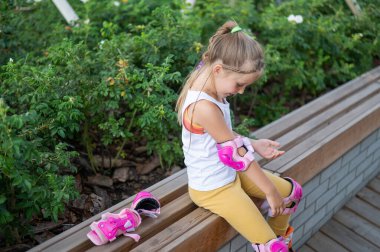 Little caucasian girl puts on protection before roller skating.