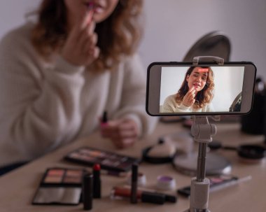 Kafkasyalı genç bir kadın cep telefonunda bir makyaj eğitimi videosu kaydediyor. Video blogcusu kız makyaj yapıyor.