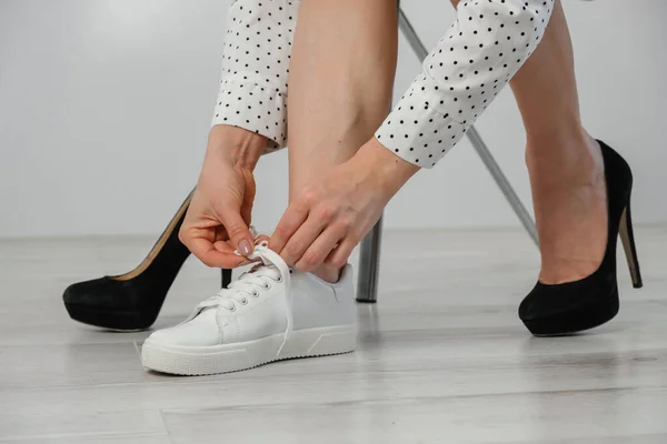 Close-up business kobieta zdejmuje buty zakłada białe skórzane trampki. — Zdjęcie stockowe