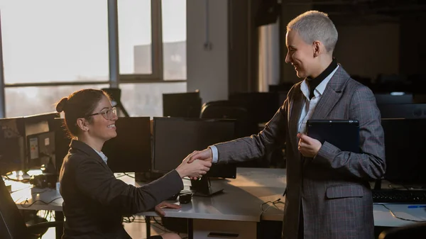 Zwei junge Geschäftsfrauen geben sich bei der Arbeit die Hand. Die Büroangestellten machten einen Deal — Stockfoto