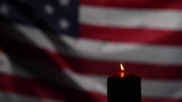 Горящая свеча на фоне размахивающего флагом Соединенных Штатов Америки в темноте. — стоковое видео