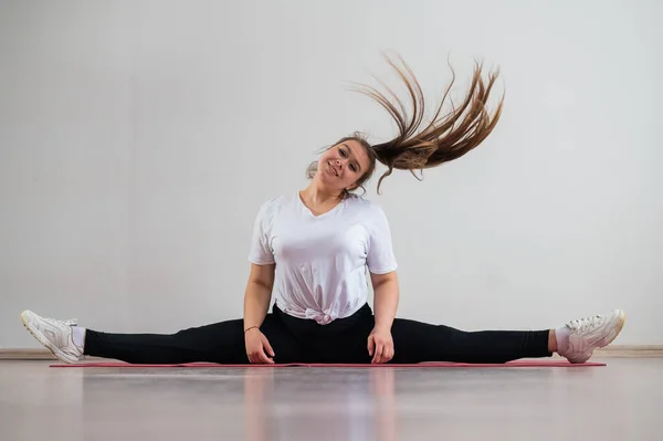 Une jeune femme grasse flexible s'assoit dans une ficelle transversale et agite ses cheveux sur un fond blanc — Photo