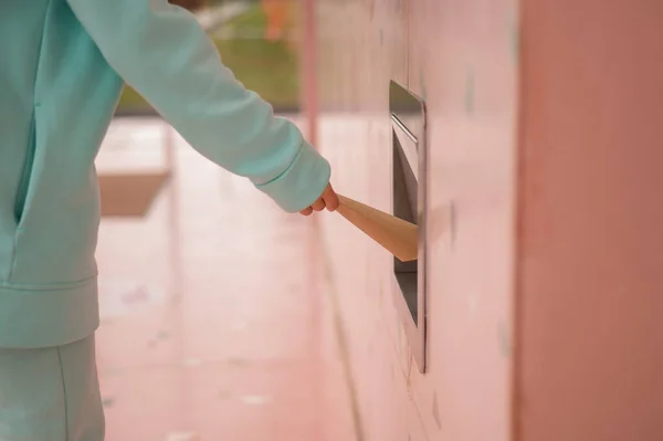 Una mujer tira una bolsa de papel kraft por un agujero de basura en la pared de un café. —  Fotos de Stock