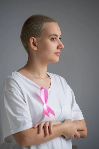 Mujer con un corto corte de pelo rubio con una cinta rosa en una camiseta blanca como símbolo de cáncer de mama sobre un fondo blanco. — Foto de Stock