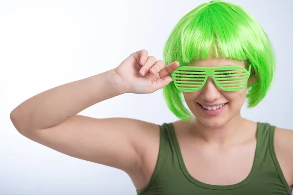 Веселая молодая женщина в зеленом парике и смешных очках празднует День святого Патрика на белом фоне — стоковое фото
