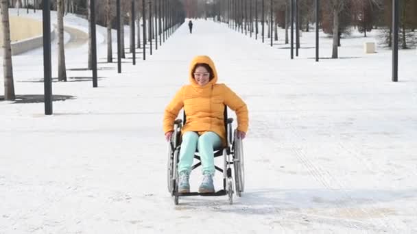 Engelli beyaz kadın kışın parkta bir sandalyeye biner. Tekerlekli sandalyede yürüyen bir kız. — Stok video