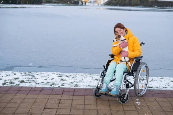 Blanke vrouw in een rolstoel laat de hond uit in de winter. — Stockfoto