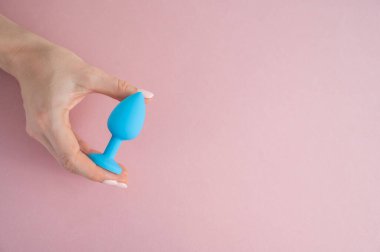 Bir kadın pembe arka planda mavi anal bir tıpa tutuyor. Alternatif seks için yetişkin oyuncağı