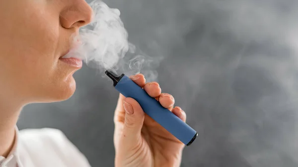 Caucasian woman smokes a disposable vape in the studio.