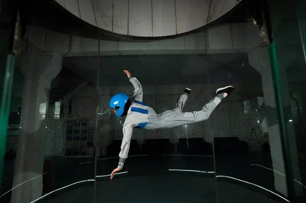 Una giovane donna in tuta e un casco protettivo gode di volare in una galleria del vento. Simulatore caduta libera — Foto Stock