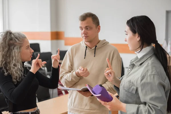 Dvě holky a chlap mluví znakovou řečí. Tři hluší studenti chatují v univerzitní třídě. — Stock fotografie